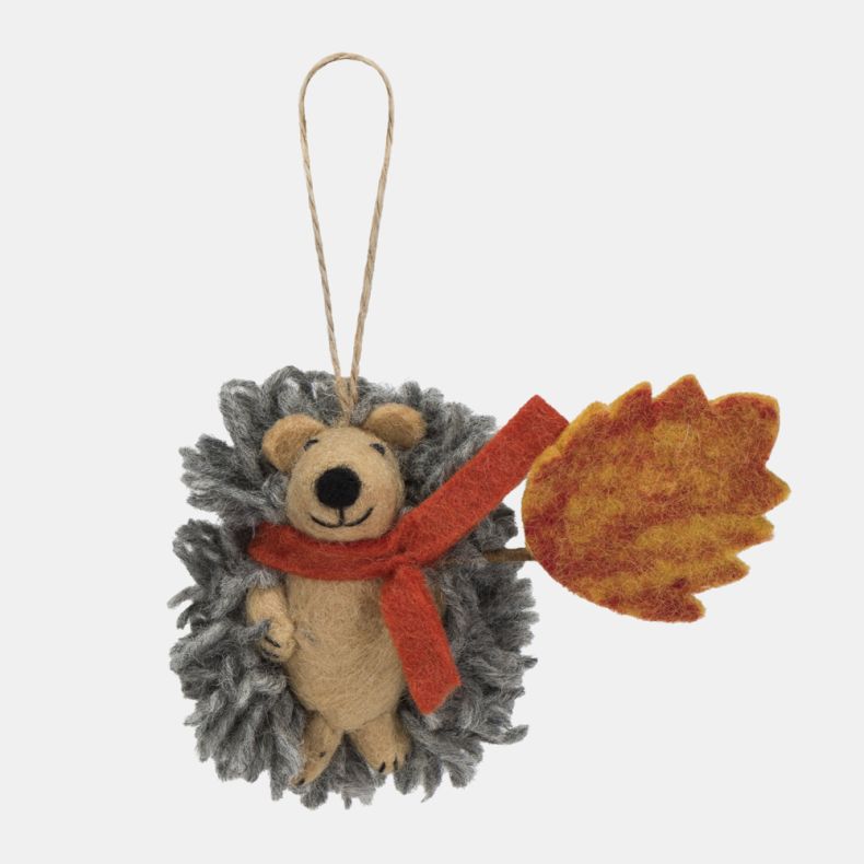 Felt hedgehog hanging decoration featuring a soft grey textured coat, beige felt face, and a bright orange scarf. Holding a large orange and yellow autumn leaf, this charming seasonal ornament is finished with a natural hanging loop and is ideal for autum