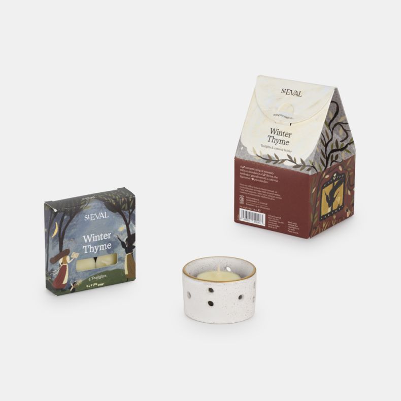 St Eval Winter Thyme scented gift set featuring four fragranced tealight candles, a white speckled ceramic tealight holder with decorative cut-out detailing, and illustrated seasonal gift packaging with woodland-inspired artwork.