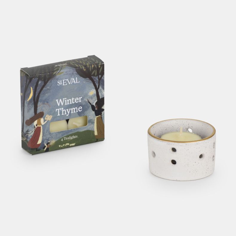 St Eval Winter Thyme scented tealight gift set featuring four fragranced tealight candles and a white speckled ceramic tealight holder with decorative cut-out detailing, presented alongside illustrated seasonal packaging.