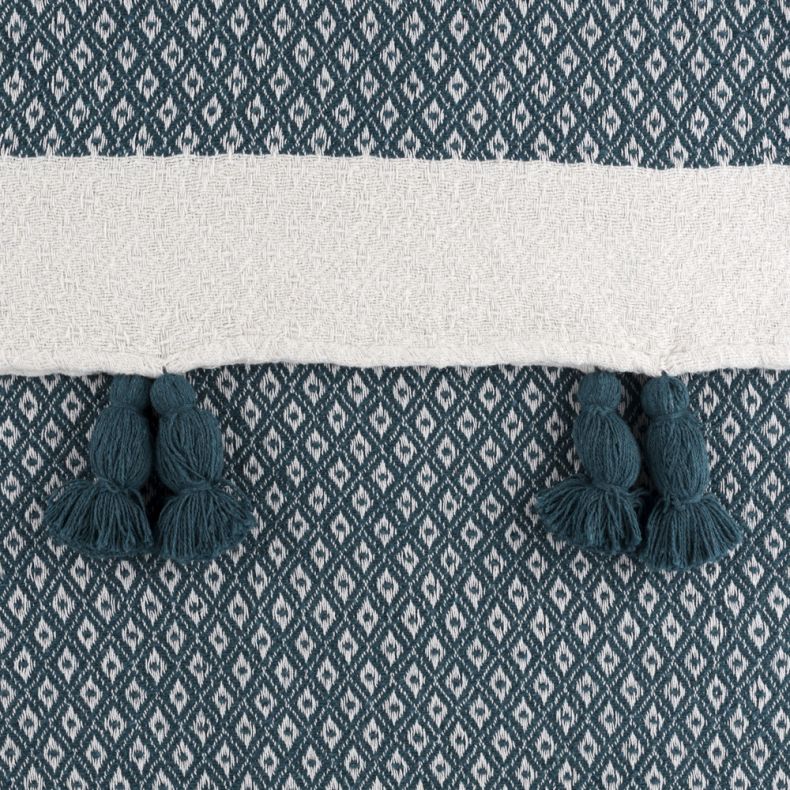 Close-up of a woven throw blanket featuring a teal and cream geometric diamond pattern. A textured cream stripe runs across the fabric, accented with teal tassels hanging along the edge. Detailed textile weave and decorative trim are clearly visible.