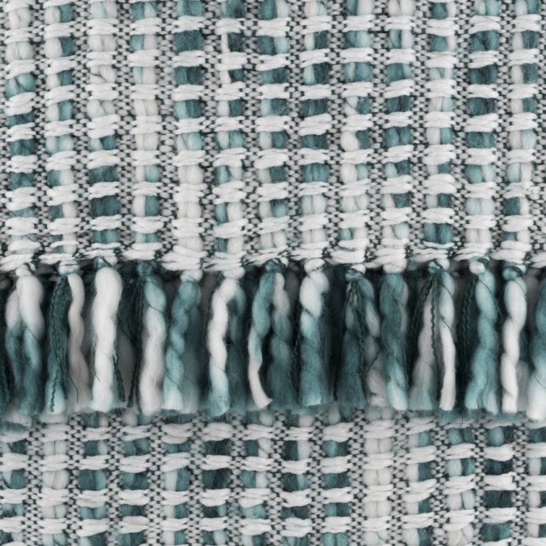 Close-up of a woven throw blanket featuring a textured teal, aqua and white basket-weave pattern with decorative tassel fringe. Thick, soft yarns create a cosy, handcrafted look, highlighting the blanket’s rich texture and detailed weave.