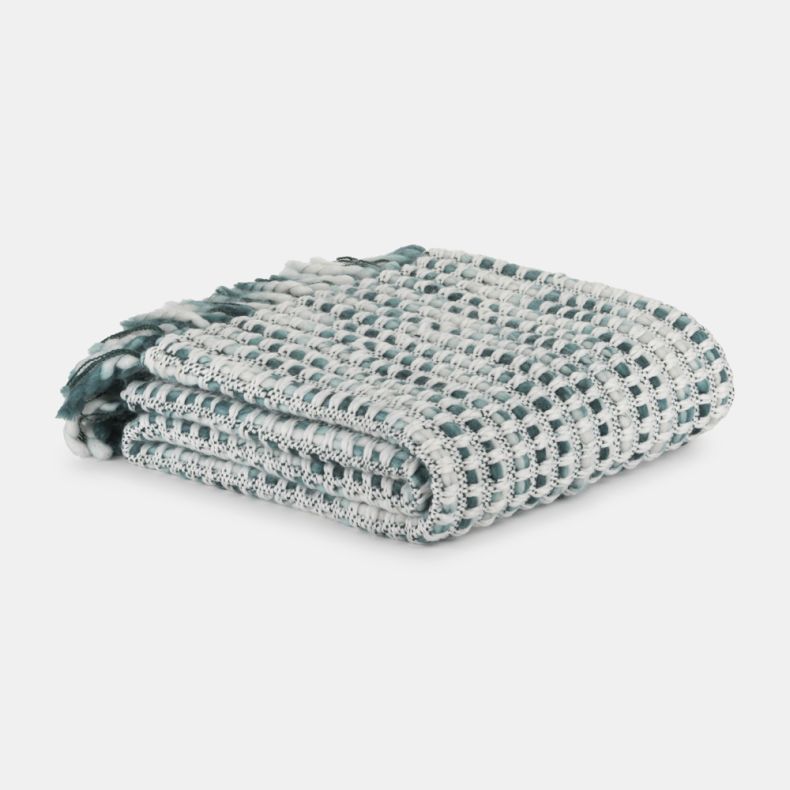 Folded teal and white woven throw blanket with a textured basket-weave pattern, neatly stacked on a light grey background. Soft fabric loops and fringe details are visible, highlighting the blanket’s cosy, handcrafted design.