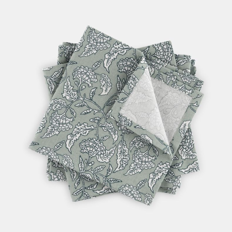 Set of Kilburn & Scott napkins in soft sage green, featuring an elegant heritage-inspired floral and bird print in contrasting white. Arranged to showcase both the front pattern and reverse side, the woven fabric highlights intricate botanical detailing a