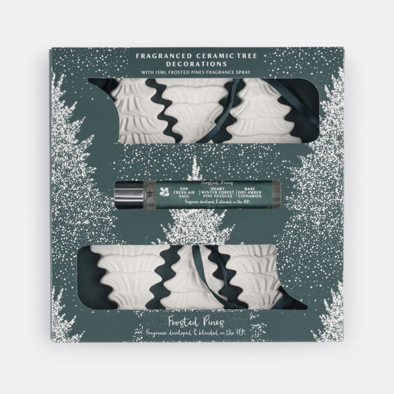 Frosted Pines fragranced ceramic tree decoration gift set featuring six white embossed Christmas tree ornaments with hanging ribbons and a 15ml festive room fragrance spray, presented in a green winter-themed gift box.