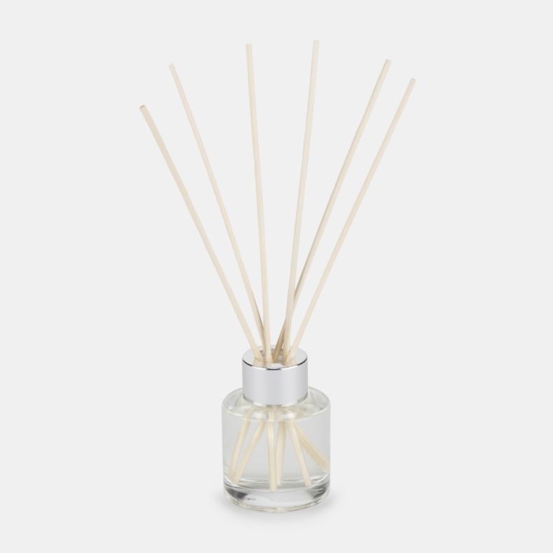Luxury reed diffuser with a clear glass fragrance bottle, silver cap, and natural reed sticks. Elegant home fragrance accessory displayed on a light background, designed to gently scent living spaces.