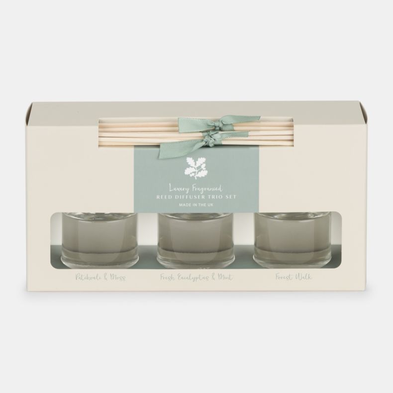 Luxury fragranced reed diffuser trio gift set featuring three glass diffusers with reeds. Scents include Patchouli & Moss, Fresh Eucalyptus & Mint, and Forest Walk, presented in a cream gift box with a soft green label and ribbon.