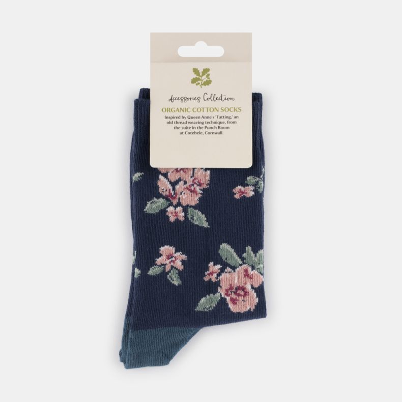 Navy blue floral organic cotton socks with soft pink flower pattern, sage green leaves, contrasting teal heel and toe, displayed folded with retail packaging.