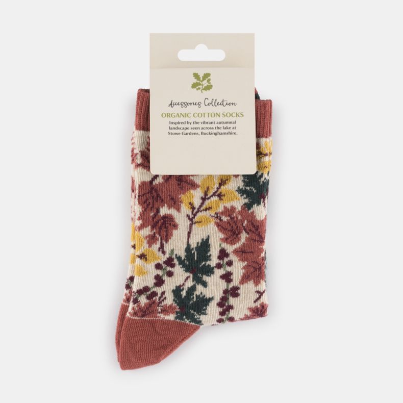 Cream botanical organic cotton socks with an autumn-inspired leaf and berry pattern, featuring rust orange cuffs, heel and toe, with yellow, burgundy and dark green foliage, displayed folded with retail packaging.