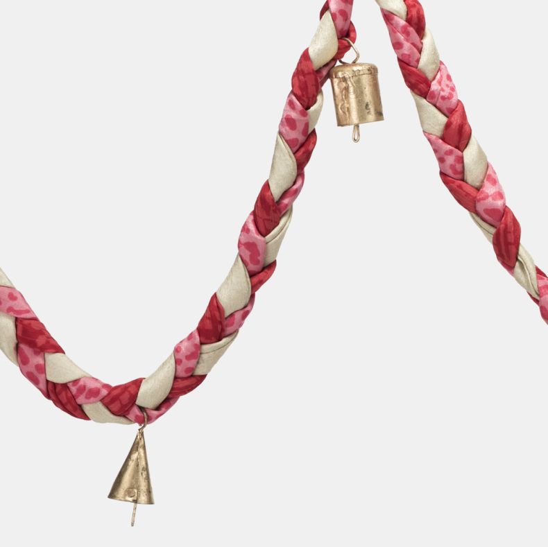 Pink and cream braided fabric garland close-up, highlighting the twisted patchwork-style fabric design in floral and patterned prints with decorative gold-tone bell charms for festive seasonal home décor.