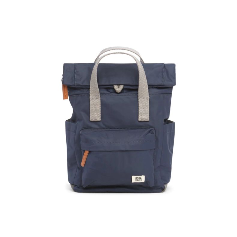 Roka London backpack in navy blue with light grey carry handles, a roll-top opening, front zip pocket, side pockets and tan zip pulls. Lightweight, practical design featuring the Roka London logo on the front pocket.