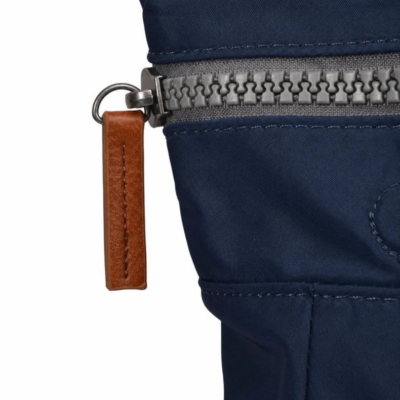 Close-up detail of a Roka London backpack, showing the navy blue water-resistant fabric, grey zip fastening and tan faux leather zip pull. The image highlights the bag’s durable materials and premium finishing details.
