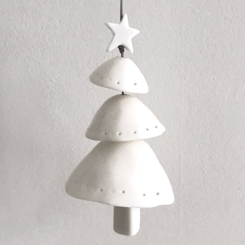 White ceramic Christmas tree hanging decoration shown in a lifestyle close-up, featuring a layered tiered tree design with a star topper, subtle pierced dot detailing, matte ceramic finish, and grey hanging cord, styled against a neutral textured backgrou