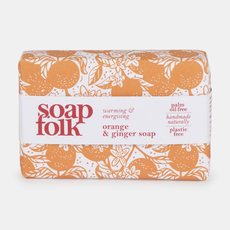 Soap Folk Orange & Ginger Soap bar in orange and white floral packaging. Label reads “warming & energising orange & ginger soap” and highlights palm oil free, handmade naturally, and plastic free features.