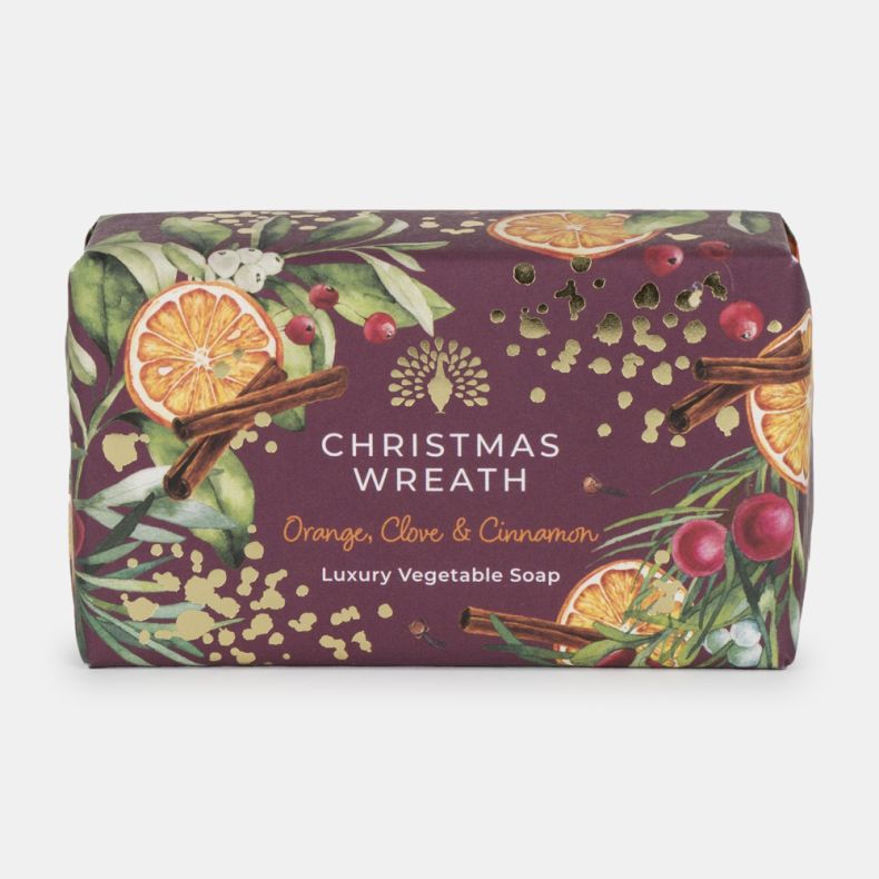 Christmas Wreath luxury vegetable soap in festive burgundy packaging decorated with dried orange slices, cinnamon sticks, red berries, greenery, and gold accents. Scented with orange, clove and cinnamon.
