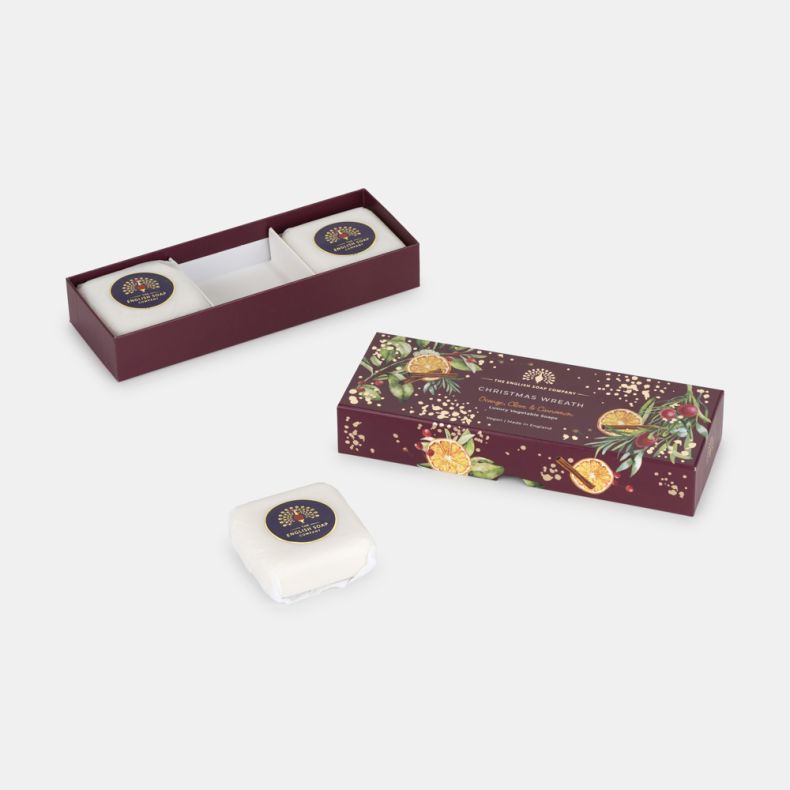 Open Christmas Wreath soap gift box with two wrapped luxury vegetable soaps inside and one soap displayed separately. Festive burgundy packaging features dried orange slices, cinnamon sticks, berries, greenery and gold accents.