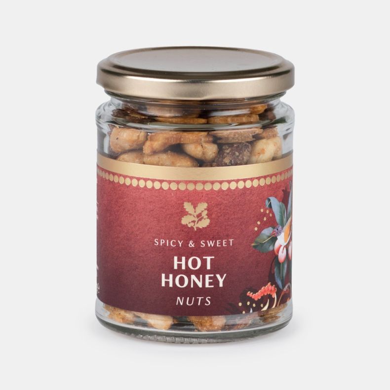 Jar of spicy and sweet hot honey nuts, featuring a clear glass jar with a gold lid and a burgundy label decorated with botanical artwork, showing honey-coated mixed nuts inside and isolated on a white background.