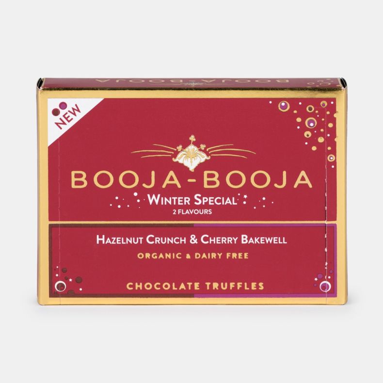 Close-up of Booja-Booja Winter Special chocolate truffles packaging, featuring red and gold festive artwork with decorative accents, highlighting Hazelnut Crunch and Cherry Bakewell flavours, organic and dairy-free chocolate truffles, displayed on a white