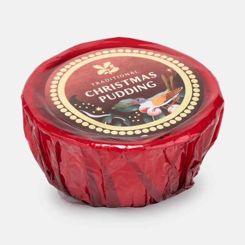 Traditional Christmas pudding wrapped in red cellophane with a festive Christmas label featuring holly leaves, berries and a bird, shown at an angled view.