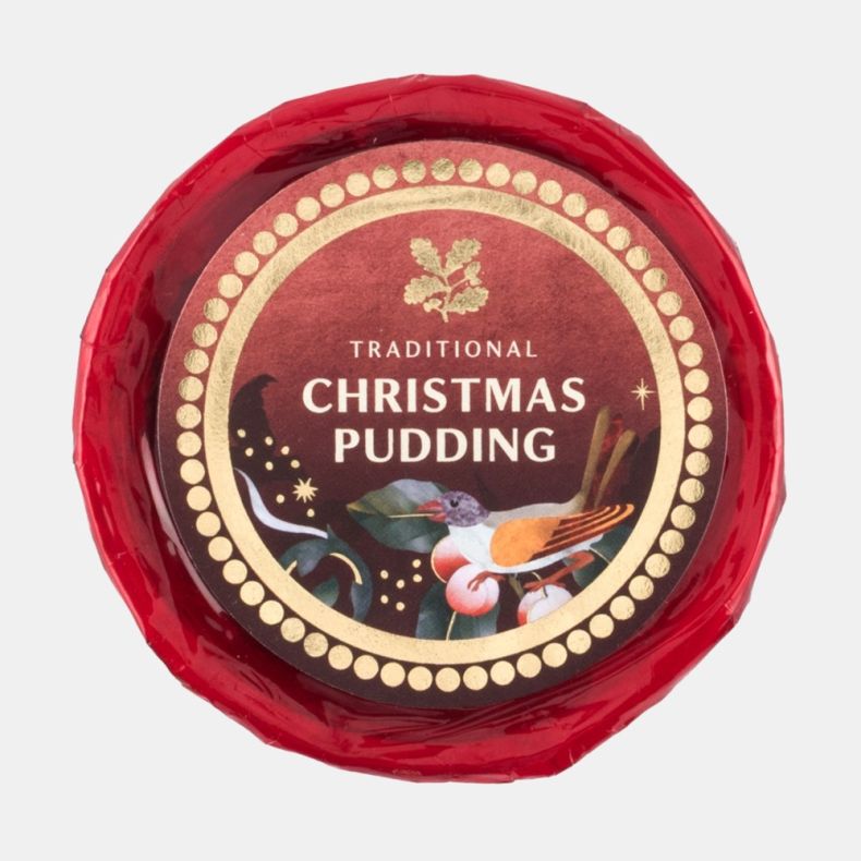 Traditional Christmas pudding wrapped in red cellophane with a festive illustrated label featuring holly, berries and a bird, viewed from above.
