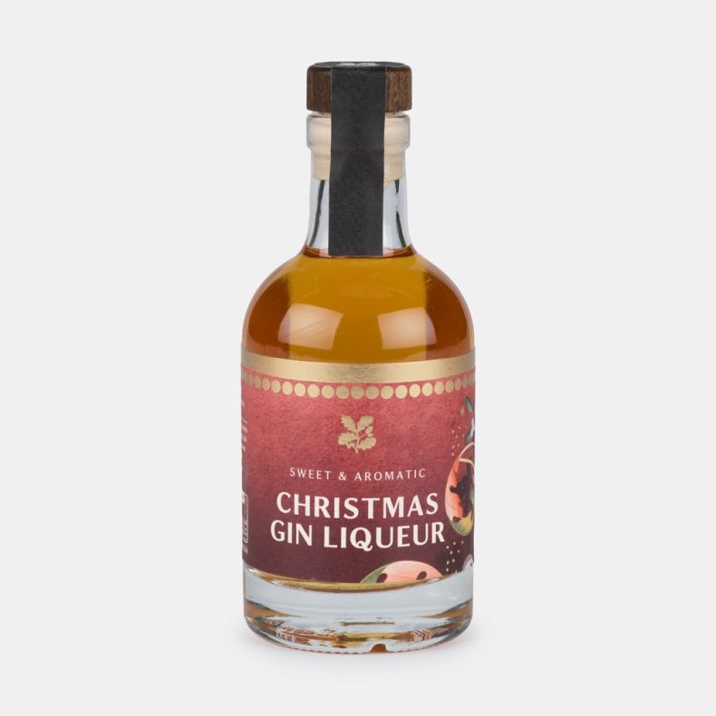 Bottle of sweet and aromatic Christmas gin liqueur with a festive illustrated label and wooden-effect stopper, presented on a light grey background.