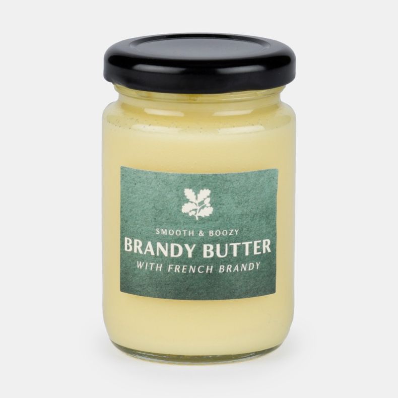 Jar of smooth and boozy brandy butter with French brandy, featuring a green label and black lid, presented on a light grey background.