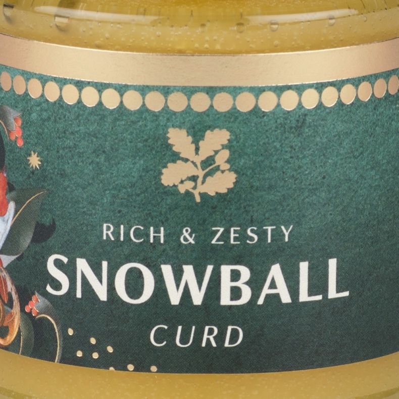 Close-up of a snowball curd jar label featuring a robin illustration and the text “Rich & Zesty Snowball Curd” on a festive green background.