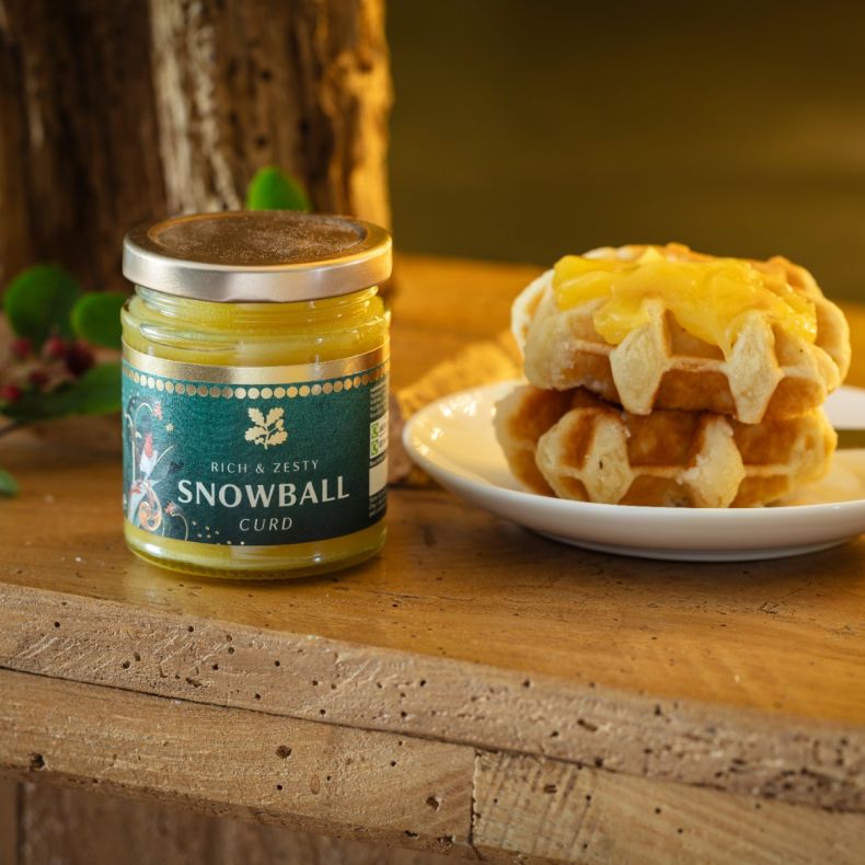 Snowball curd in a glass jar with a silver screw-top lid, displayed alongside golden waffles topped with curd on a white plate to showcase the rich, zesty flavour and serving suggestion.