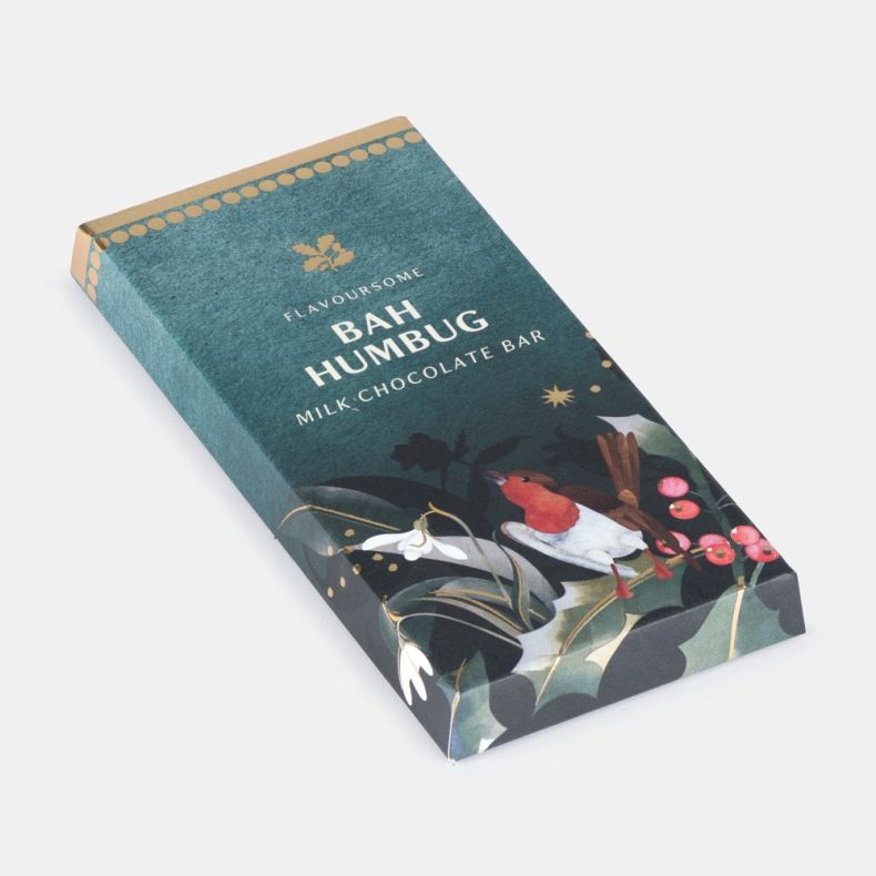 Bah Humbug milk chocolate bar in festive packaging featuring a robin, holly leaves, red berries and snowdrops on a dark green background, displayed at an angled view.
