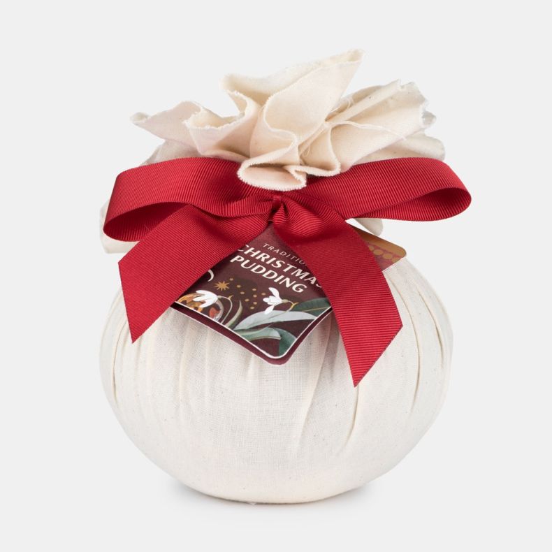 Traditional Christmas pudding wrapped in natural cloth with a red ribbon bow and festive gift tag, presented on a light grey background.