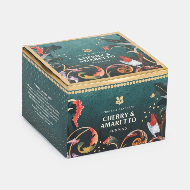 Cherry & amaretto pudding in a festive teal presentation box featuring robin and botanical illustrations with gold accents, shown at an angled view.