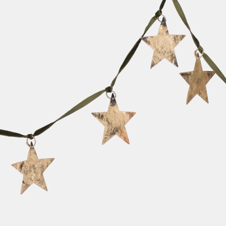Close-up of decorative star garland featuring hammered metal star ornaments in a distressed antique gold finish suspended from an olive green ribbon, showcasing the textured metallic detailing and handcrafted appearance.