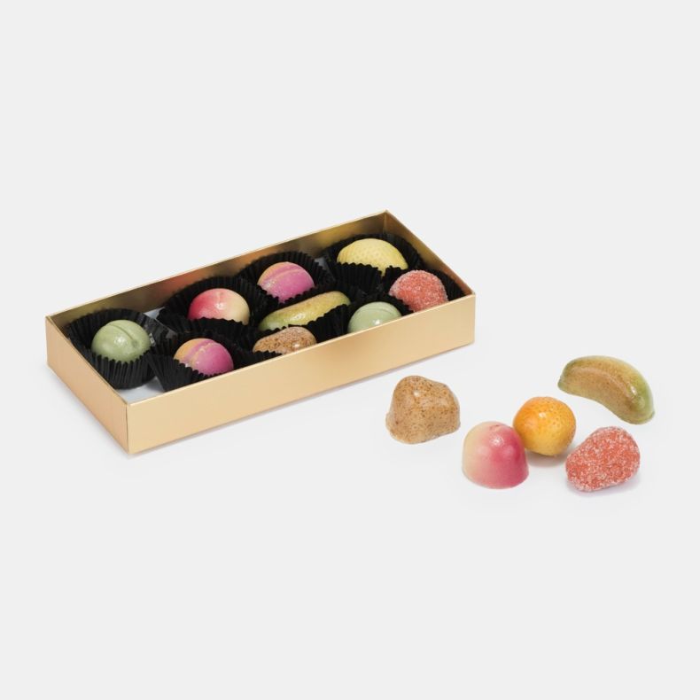 Assorted fruit-flavoured confectionery sweets in a gold presentation tray, featuring a variety of colourful shapes and finishes, displayed alongside selected sweets on a light grey background.
