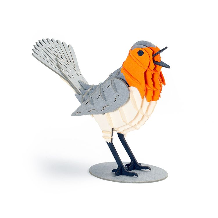 Assembled 3D robin puzzle model standing on a round base, featuring layered grey, white, and bright orange pieces that create a detailed bird shape with raised wings, tail feathers, and black legs against a plain light background.