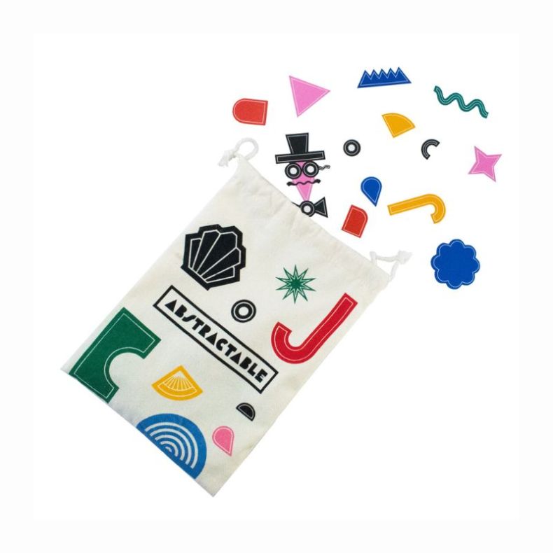 Abstractable drawstring storage bag beside colourful geometric shape pieces used in the game, including stars, curves, triangles and other abstract forms. The bag features the Abstractable logo and matching graphic design elements.