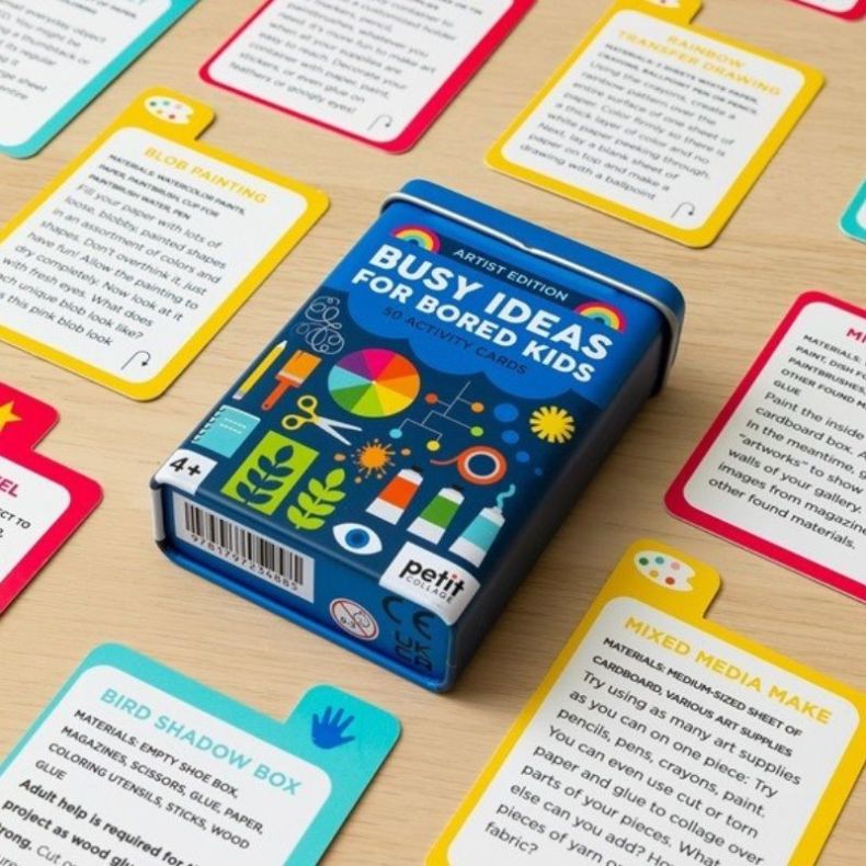 Petit Collage Busy Ideas for Bored Kids Artist Edition displayed with its blue storage tin and colourful activity cards spread across a tabletop, showcasing creative art, craft and drawing prompts for children aged 4+.