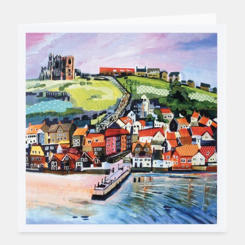 Landscape-themed notecard featuring colourful artwork of a coastal harbour town with rows of red-roofed houses beside the waterfront, a long staircase leading up a green hillside to a historic abbey, and calm water in the foreground, displayed with a whit