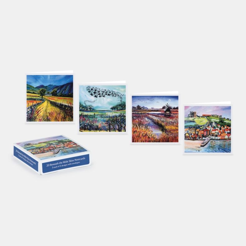 Collection of 20 Beneath the Wide Skies notecards with envelopes, displayed alongside four landscape-themed card designs featuring countryside scenes, wetlands with birds, a windmill by a river, and a coastal harbour town, presented with the branded stora