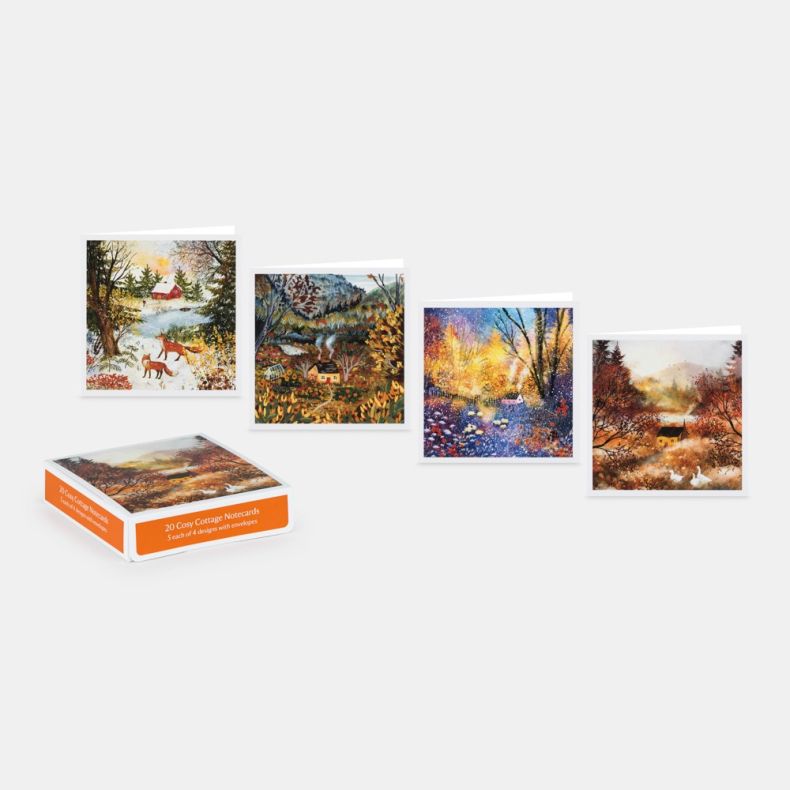 Collection of 20 Cosy Cottage notecards with envelopes, displayed alongside four cottage-themed card designs featuring seasonal countryside scenes with cottages, woodland landscapes, wildlife and colourful foliage, presented with the branded storage box o
