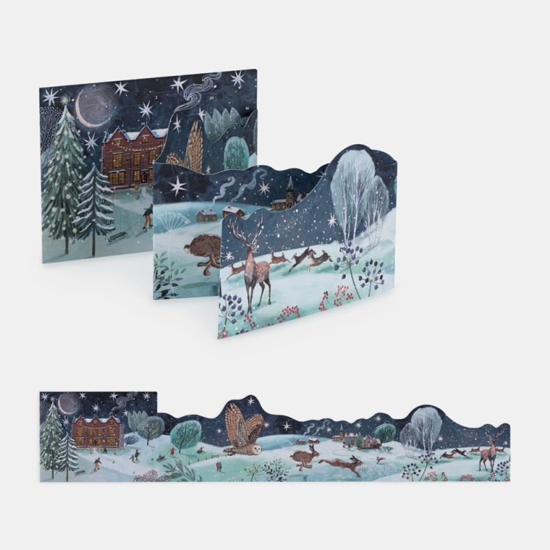 Freestanding advent calendar shown both partially assembled and fully extended, featuring a panoramic winter countryside illustration with a grand house, deer, hares, an owl in flight, snow-covered trees, village cottages and people enjoying seasonal outd