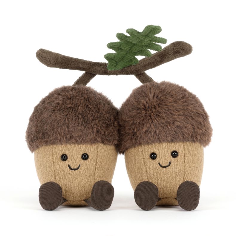 Jellycat acorn soft toy featuring two smiling plush acorns joined by a soft branch with green oak leaves. The cuddly woodland duo has fluffy brown caps, tan bodies, corduroy legs and embroidered facial details.