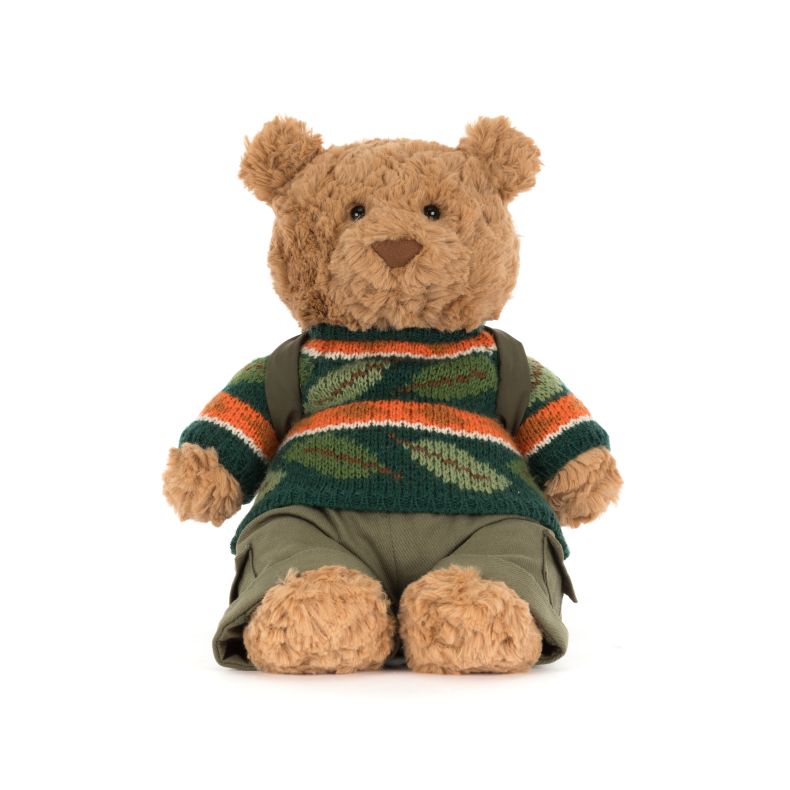 Jellycat teddy bear plush dressed for adventure, featuring soft beige fur, a green camouflage-style knitted sweater with orange and white stripes, khaki trousers, and a backpack. The bear is seated against a plain light background.