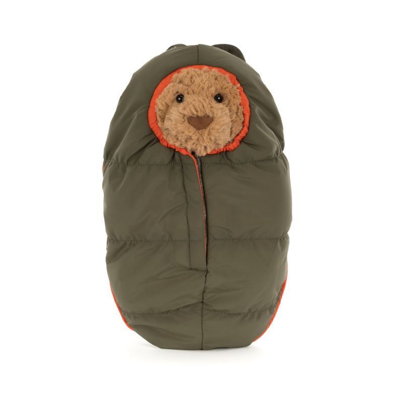 Jellycat teddy bear plush tucked inside an olive-green padded sleeping bag with bright orange trim. Only the bear’s face is visible through the hood opening, creating a cosy camping-themed look against a plain light background.
