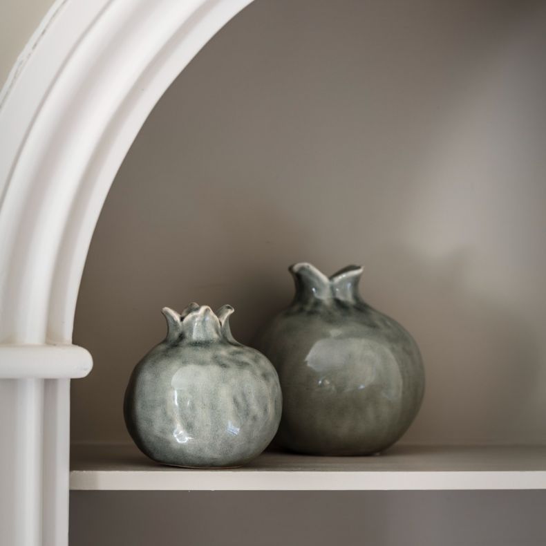 Two decorative ceramic vases displayed on a built-in shelf beneath a white arched alcove. The vases feature rounded, pomegranate-inspired silhouettes with distinctive crown-shaped openings and a glossy blue-grey glaze with subtle tonal variations and a de