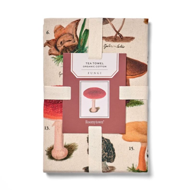 Organic cotton tea towel featuring vintage-style botanical mushroom illustrations in natural earthy tones. Folded and secured with a branded paper sleeve, the design showcases a variety of fungi species printed on a natural cream background against a plai