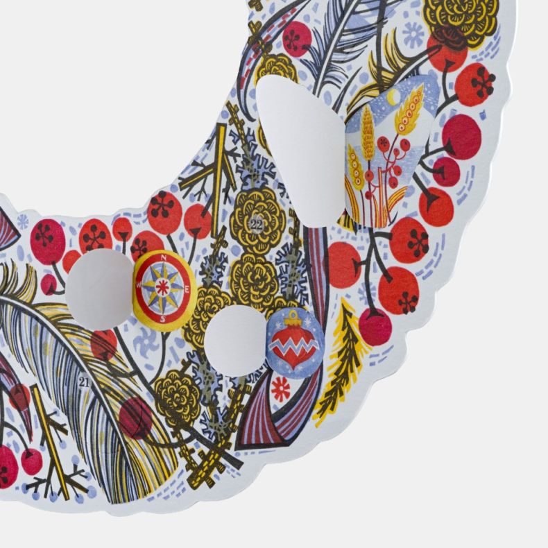 Close-up of wreath-shaped advent calendar with opening numbered doors revealing festive illustrations among winter berries, feathers and foliage designs