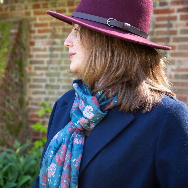 Blue floral scarf with pink and red floral print, styled around the neck with a navy coat and burgundy hat.