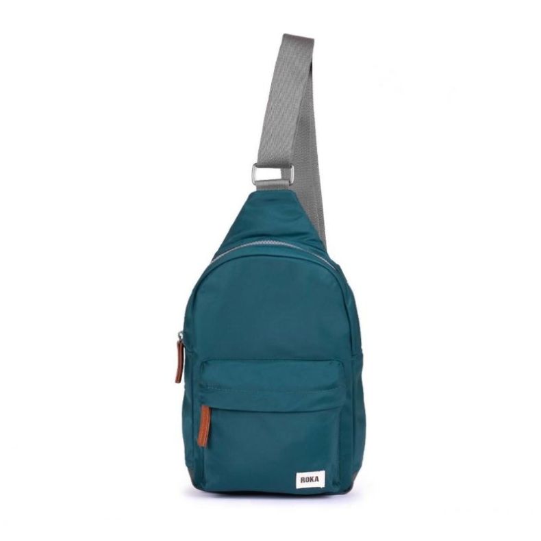 Teal sling backpack with a wide grey shoulder strap, front zip pocket, and brown zip pull tabs.
