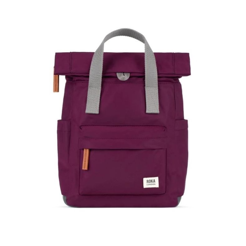 Burgundy red Roka London backpack with a roll-top closure, grey webbing carry handles, front zip pocket, side pockets, and tan zip pulls. The lightweight backpack features a minimalist design and Roka London logo label on the front.