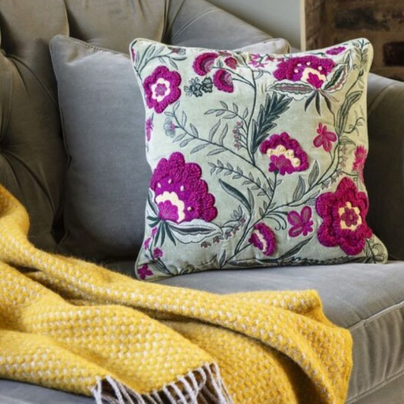Green embordered cushion and yellow throw on a sage sofa