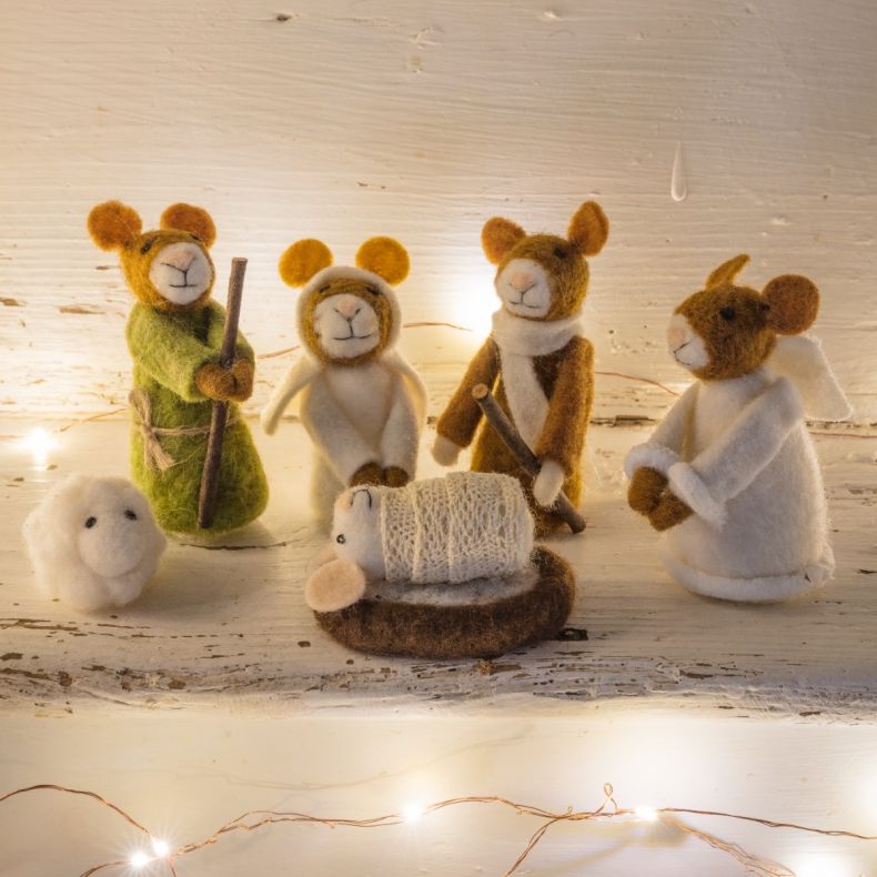 Felt nativity scene featuring handcrafted mouse characters dressed as Mary, Joseph and the baby Jesus, with a small sheep figure and rustic felt manger, displayed on a wooden shelf among warm white fairy lights for festive Christmas décor.